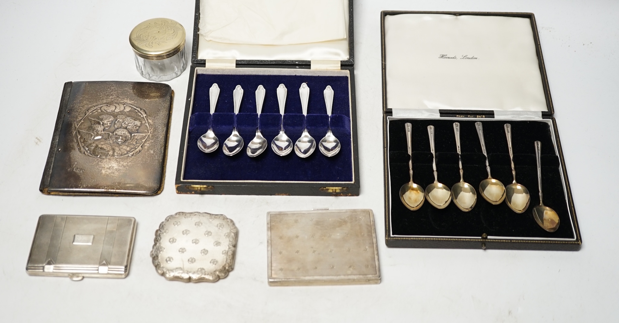 Two cased sets of six silver coffee spoons, a silver mounted leather case, two white metal cigarette cases, a white metal compact and a toilet jar. Condition - poor to fair